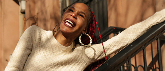 Persona sonriente usando un arete de pie en las escaleras de arenisca en la Ciudad de Nueva York.